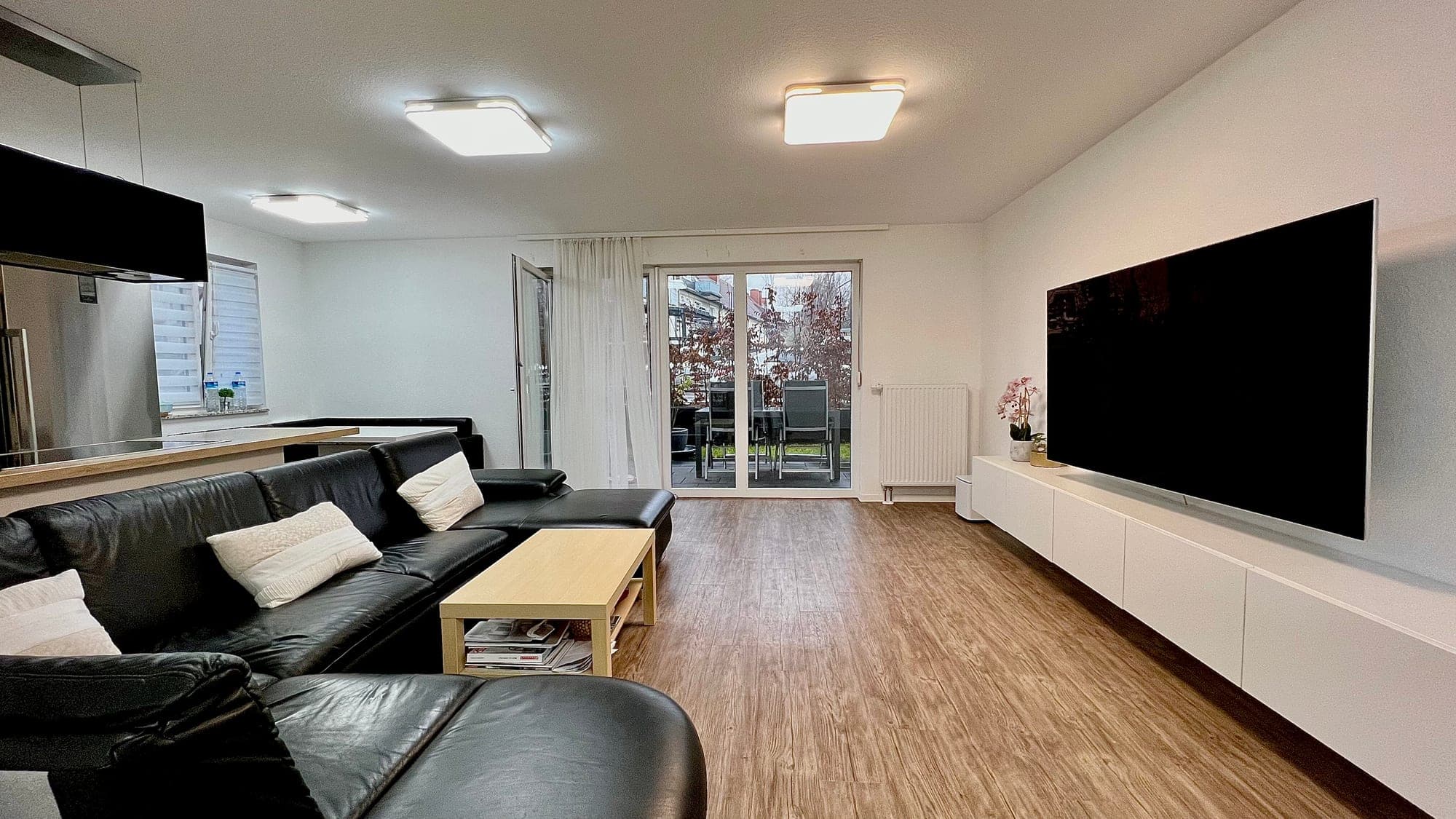 Wohnzimmer einer Wohnung mit Sofa, Fernsehwand und Terrassentür