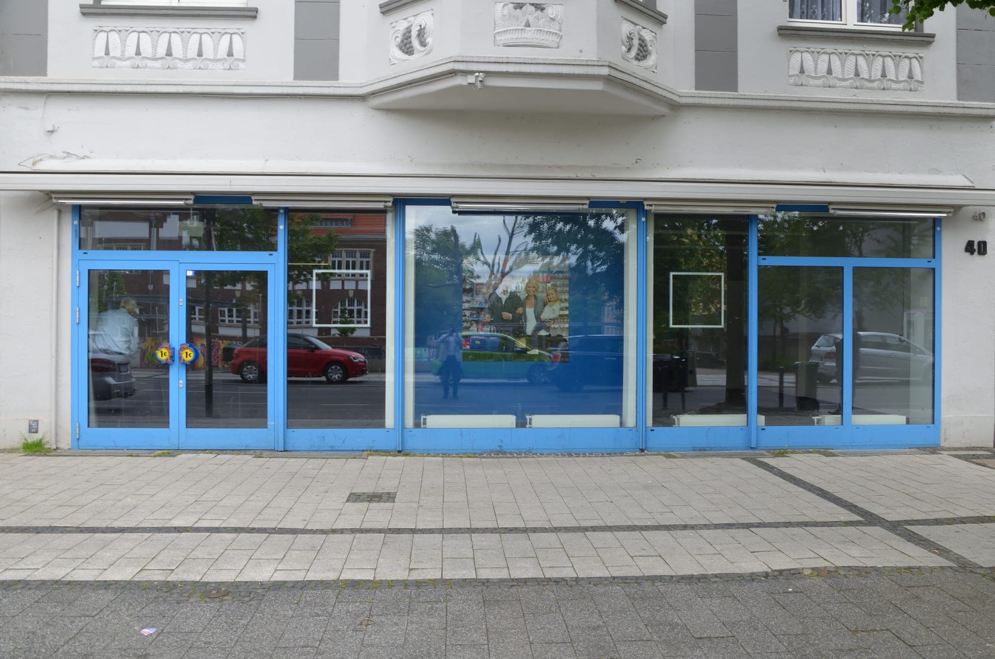 Leerstehendes Ladenlokal mit blauer Schaufensterfront, davor ein breiter gepflasterter Gehweg